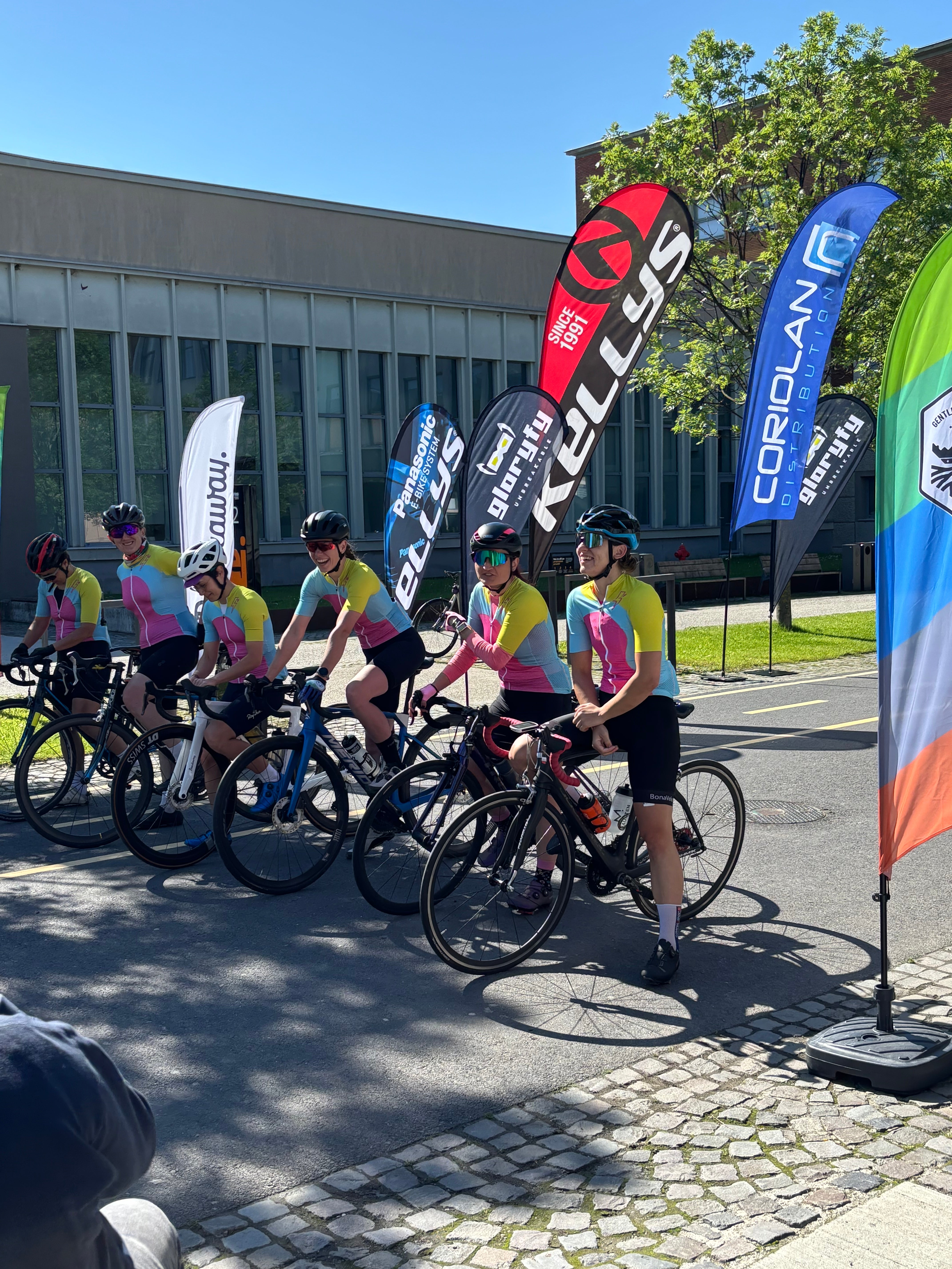 Group of cyclists with bicycles on a street, surrounded by various brand banners.